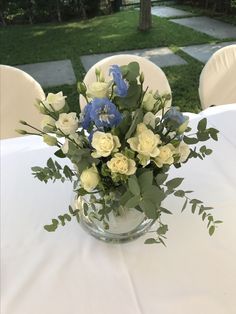 a vase filled with blue and white flowers on top of a table next to chairs