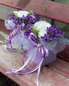 two purple and white flowers in a box on a bench with ribbon tied around it