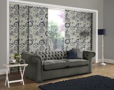 a grey couch sitting in front of a window next to a rug on top of a hard wood floor