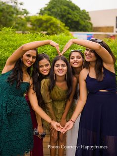 four young women are making a heart shape with their hands while posing for the camera