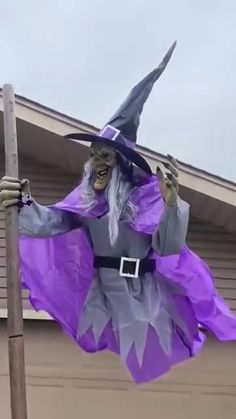 a scarecrow dressed in purple and grey holding a sign with his hands up to the side