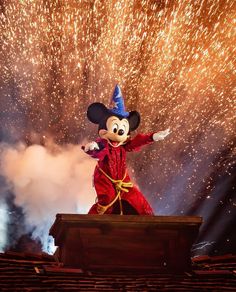 mickey mouse on stage with fireworks in the sky behind him and his arms outstretched out