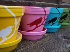 colorful flower pots are lined up on a wooden bench with birds painted on the cups