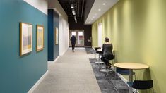 a woman sitting at a table in an office hallway with two people walking by the wall