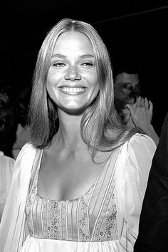 a black and white photo of a woman in a dress smiling at the camera with other people behind her