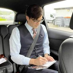 a man sitting in the back seat of a car while writing on a piece of paper