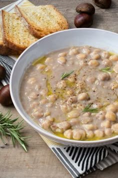 a white bowl filled with soup next to bread and olives on a wooden table