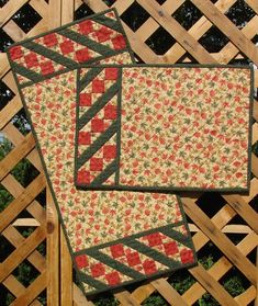 two quilted place mats sitting on top of a wooden fence