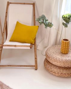 a chair with a yellow pillow on it next to a potted plant and a wicker stool