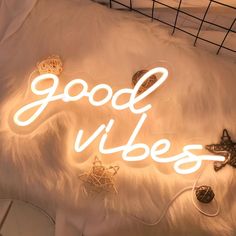 a neon sign that reads, good vibes on top of a white fur covered bed