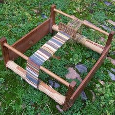 an old weaving loom is sitting in the grass on some rocks and plants,