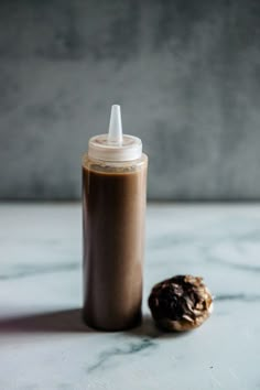 a bottle with a cap sitting next to a cookie on a marble counter top,