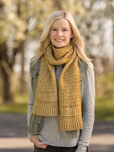 a woman wearing a yellow knitted scarf standing in front of a tree with her hands in her pockets