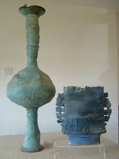 two vases sitting on top of a table next to each other in front of a white wall