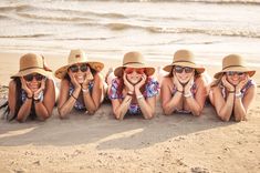 four women in hats and sunglasses laying on the beach with their hands behind their heads