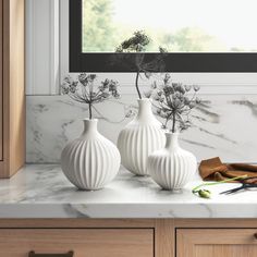 three white vases sitting on top of a counter