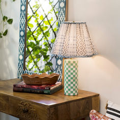 a table with a lamp, books and a basket on it in front of a window