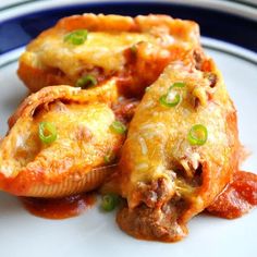 three stuffed shells are on a plate with sauce and green onions in the bottom half