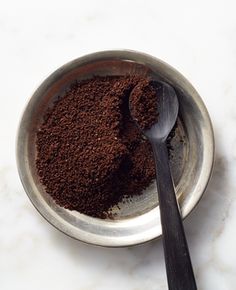 a bowl filled with ground coffee next to a spoon on top of a white counter