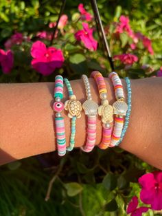 a woman's arm with several bracelets on it and flowers in the background