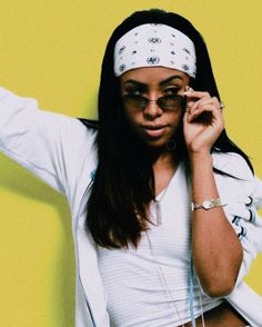 a woman with glasses and headband holding her hand up to her ear while standing in front of a yellow wall