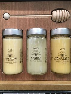 three jars of honey sitting on top of a wooden shelf