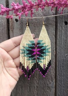 a pair of handmade beaded earrings hanging from a string on a wooden fence