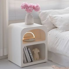 a white shelf with books and a pink flower in it next to a bed on the floor