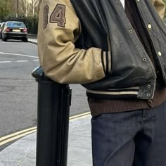 a man standing next to a pole wearing a leather jacket and hat with his hands on his hips