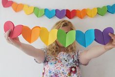 a woman standing in front of a wall with paper hearts hanging from it's sides