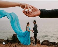 a man and woman standing next to each other near the ocean with their hands touching