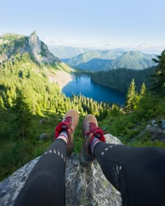 someone is standing on top of a rock with their feet in the air and looking down at a lake