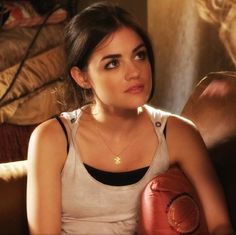 a woman sitting on a couch holding a red boxing glove in her right hand and looking at the camera