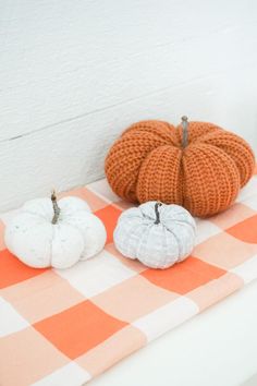 three knit pumpkins sitting on top of a checkered tablecloth with one white pumpkin in the middle