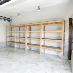 an empty room with wooden shelves in the middle and white marble flooring on the other side