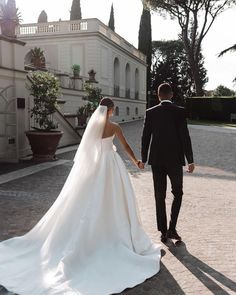 a bride and groom holding hands in front of a large white building on a sunny day