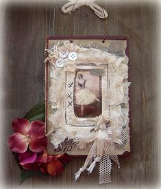 an old photo frame with buttons and lace on it next to a red flower arrangement