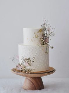 a three tiered white cake with flowers on the top and bottom, sitting on a wooden stand