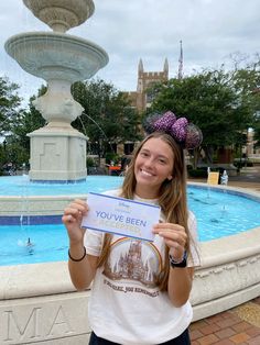 a woman holding up a sign in front of a fountain