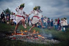 two women in white dresses jumping over a campfire while people watch from the other side