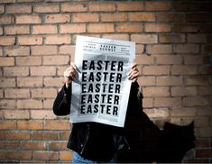 a person holding up a newspaper with the words easter written on it in front of a brick wall