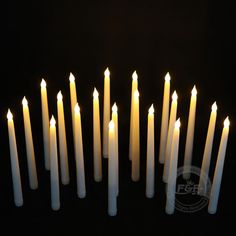 many white candles are arranged in a row on a black surface with one candle lit up