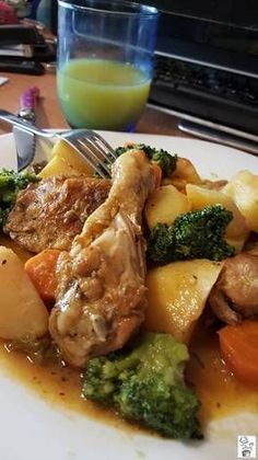 a white plate topped with meat and veggies next to a glass of orange juice