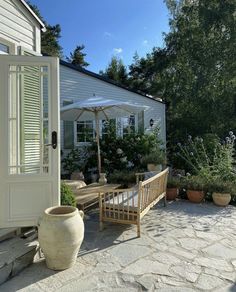 an outdoor patio with potted plants and a wooden bench in front of a white house