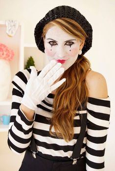 a woman with makeup on her face is posing for the camera while wearing a striped shirt and black hat