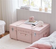 a pink suitcase sitting on top of a bed next to a white rug and window