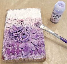 a piece of fabric with purple flowers on it next to a paintbrush and glue