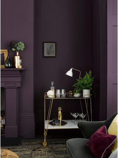 a moody living room with an aubergine accent wall, a fireplace, a delicate gold bar cart and a black sofa with colorful pillows Deep Purple Wall Color, Deep Purple Room Ideas, Dark Purple Wall Paint, Deep Purple Walls, Eggplant Paint Color, Dark Purple Living Room, Dark Purple Room, Dark Purple Bedroom, Dark Purple Wall