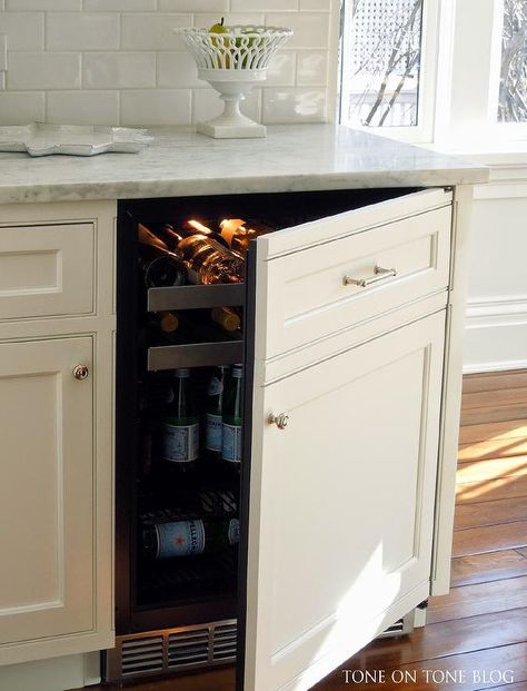 Kitchen features creamy white cabinets fitted with a white paneled beverage fridge with pull out wine trays paired with carrera marble countertops and a glazed white subway tiled backsplash. Hidden Wine Fridge Cabinet, Hidden Drink Fridge, Under Counter Wine Fridge In Kitchen, Inside Cabinet Wine Storage, Corner Wine Fridge, Paneled Mini Fridge, Beverage Refrigerator Cabinet, Fridge That Blends In With Cabinets, Hidden Wine Fridge