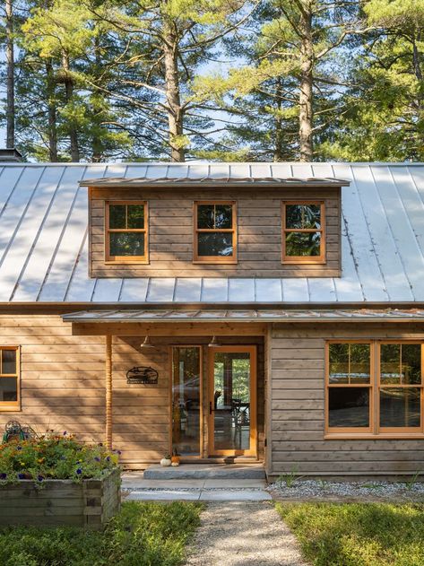 Cedar wood exterior siding with a brown stain keeps this Maine summer camp camouflaged in its surroundings. Orange hemlock posts and trim provide a contemporary chic touch while maintaining the rustic inspiration. Cedar Contemporary House, Cedar Shake Cabin, Contemporary Rustic Exterior, Maine Modern Cabin, Brown Cedar House Exterior, Horizontal Wood Siding Exterior, Lake Cabin Exterior Colors, Cabin In The Woods Exterior, Stained Wood House Exterior